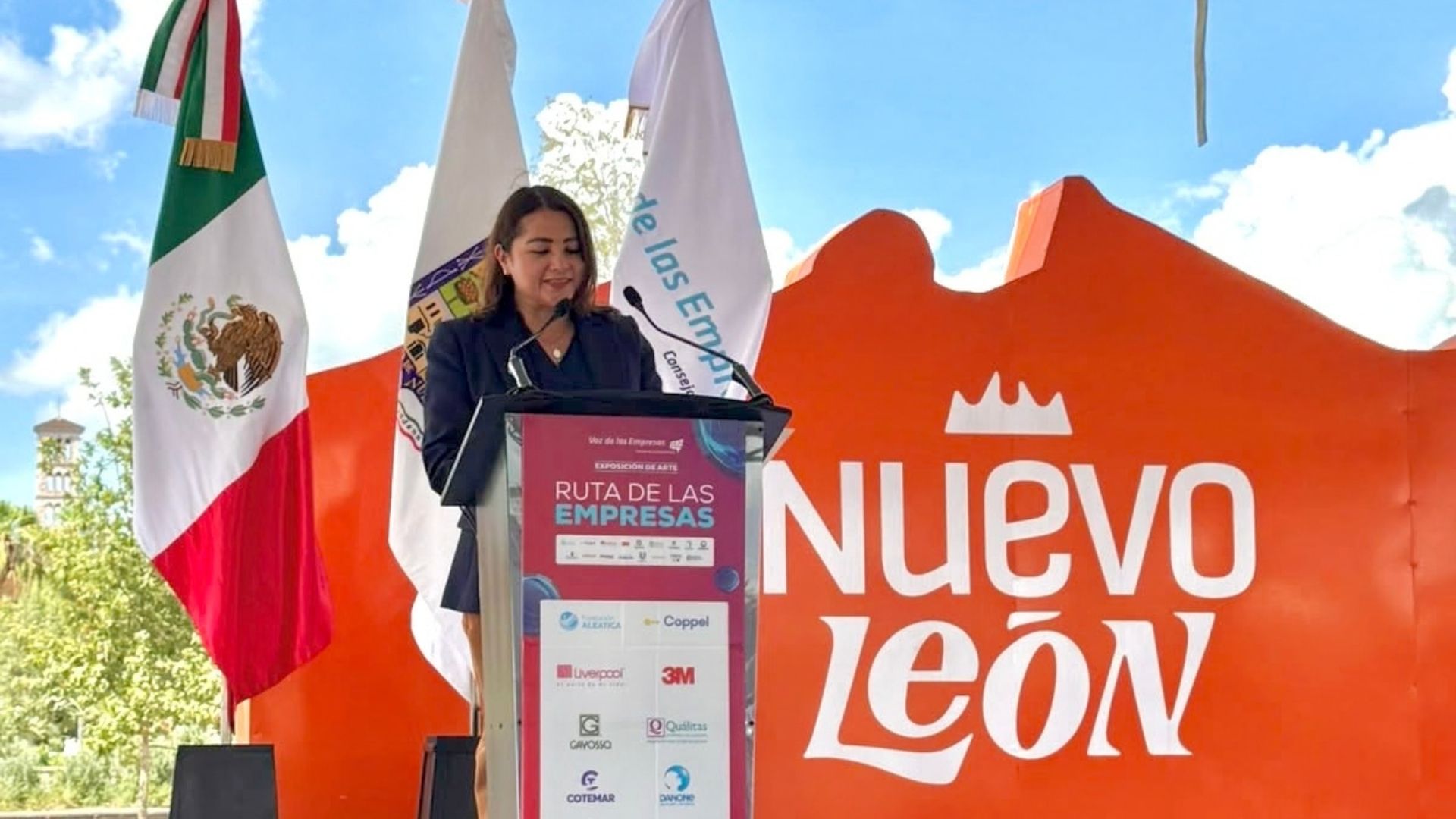 Una mujer habla en un podio de Ruta de las Empresas junto a la bandera mexicana y un letrero de Nuevo León.